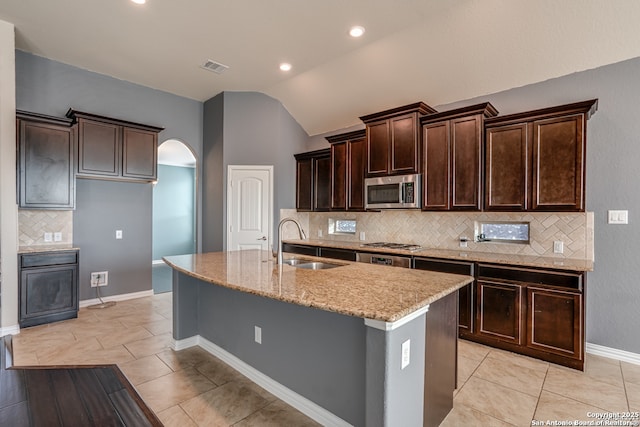 kitchen with arched walkways, stainless steel appliances, visible vents, a sink, and an island with sink