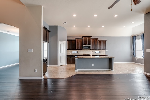 kitchen featuring arched walkways, a sink, visible vents, stainless steel microwave, and an island with sink