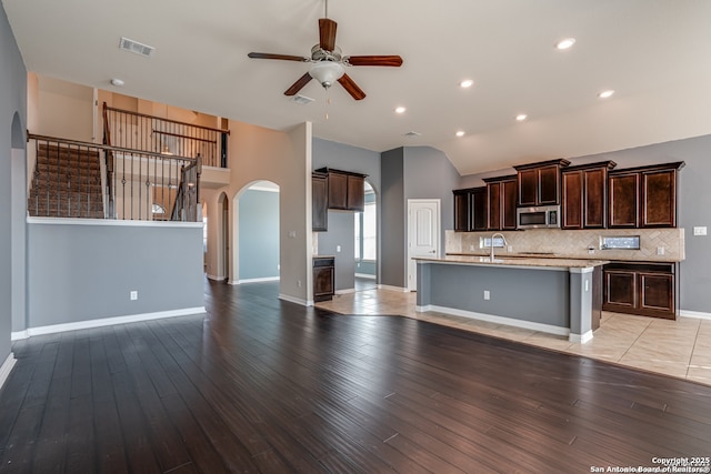 kitchen featuring dark brown cabinetry, visible vents, arched walkways, stainless steel microwave, and light countertops