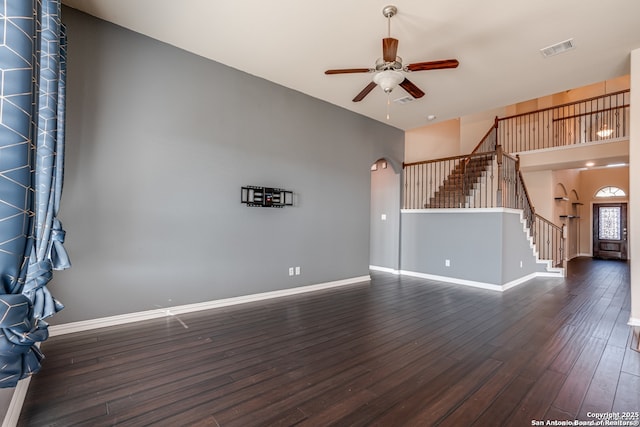 unfurnished living room featuring visible vents, arched walkways, baseboards, dark wood-style floors, and stairway