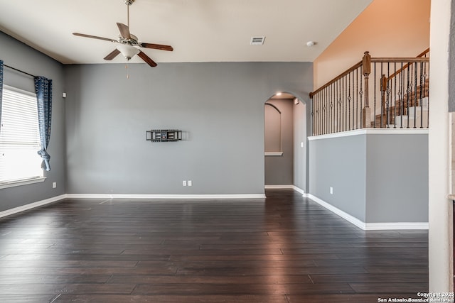 unfurnished room with arched walkways, dark wood-style flooring, visible vents, and baseboards