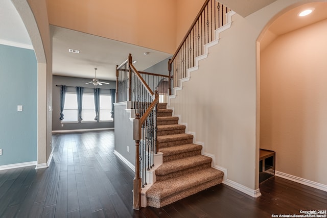 stairway with wood-type flooring, visible vents, arched walkways, and baseboards