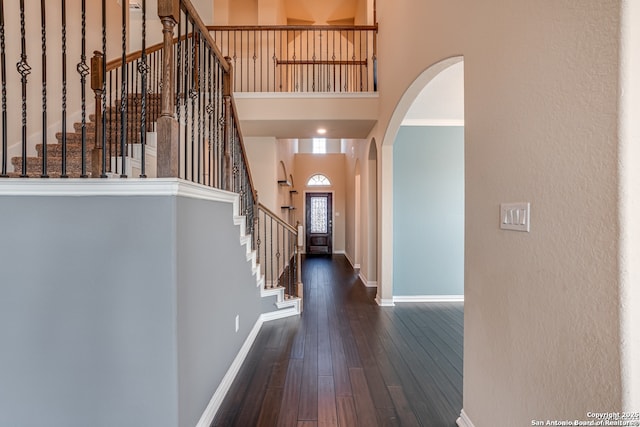 entryway with arched walkways, dark wood-style flooring, stairway, a high ceiling, and baseboards