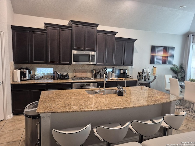 kitchen featuring light tile patterned floors, tasteful backsplash, appliances with stainless steel finishes, a kitchen island with sink, and a sink