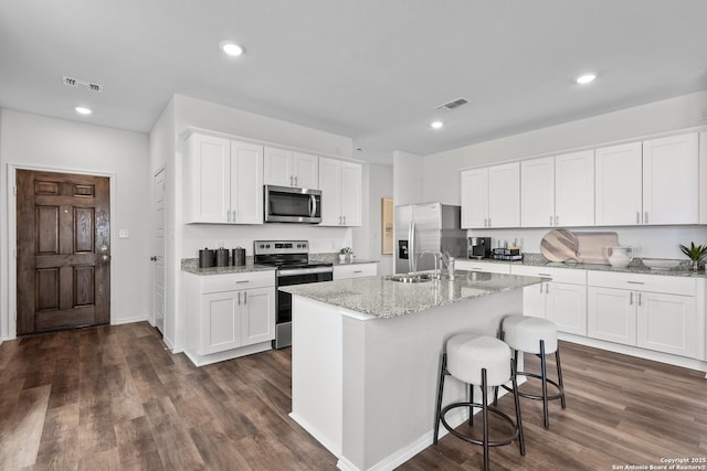kitchen with appliances with stainless steel finishes, an island with sink, sink, white cabinets, and light stone counters