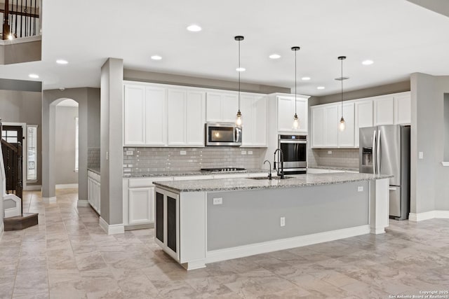 kitchen with white cabinetry, hanging light fixtures, stainless steel appliances, light stone counters, and a center island with sink