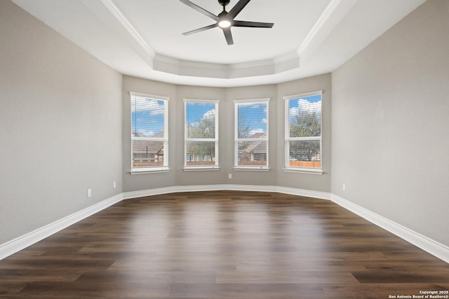 empty room with a healthy amount of sunlight, dark wood-type flooring, ceiling fan, and a tray ceiling