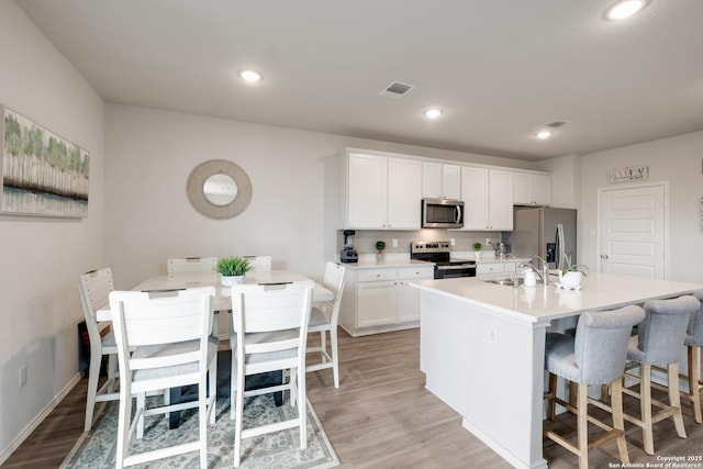 kitchen featuring appliances with stainless steel finishes, white cabinetry, an island with sink, a kitchen bar, and light wood-type flooring