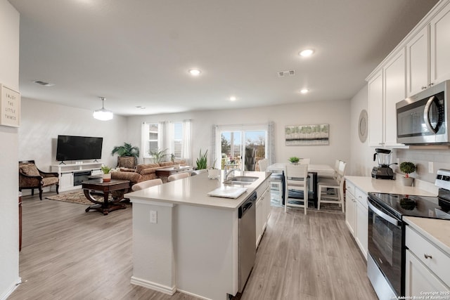 kitchen with appliances with stainless steel finishes, sink, white cabinets, a kitchen island with sink, and light wood-type flooring