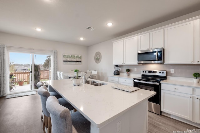 kitchen with sink, appliances with stainless steel finishes, white cabinetry, tasteful backsplash, and a center island with sink