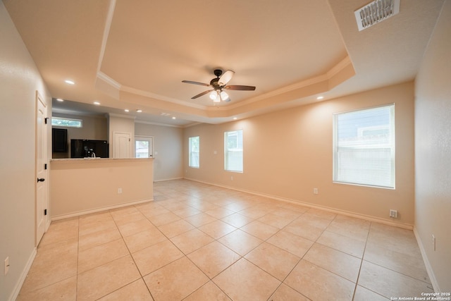 empty room featuring crown molding, a tray ceiling, and light tile patterned flooring