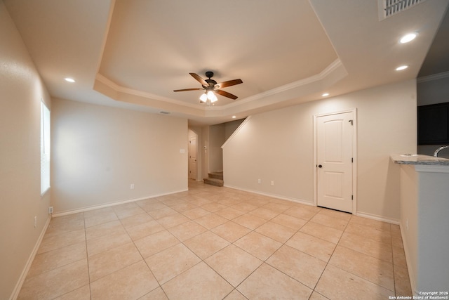 tiled empty room with ornamental molding, ceiling fan, and a tray ceiling