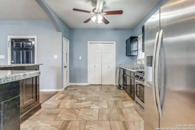 kitchen featuring light stone counters, ceiling fan, appliances with stainless steel finishes, and sink