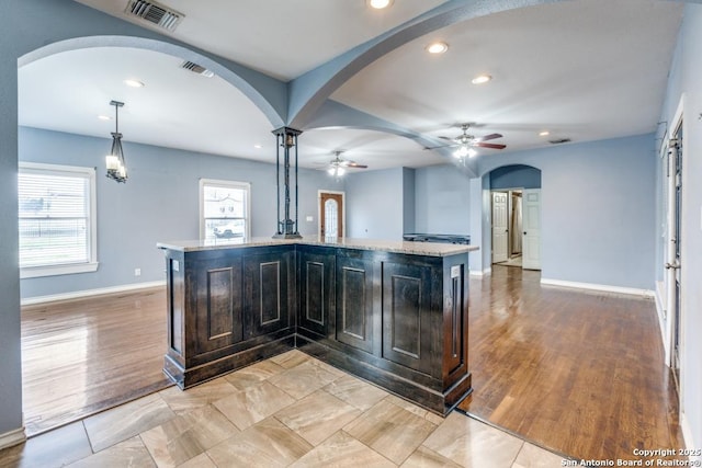 kitchen with light hardwood / wood-style flooring, ceiling fan, light stone counters, a center island with sink, and decorative light fixtures