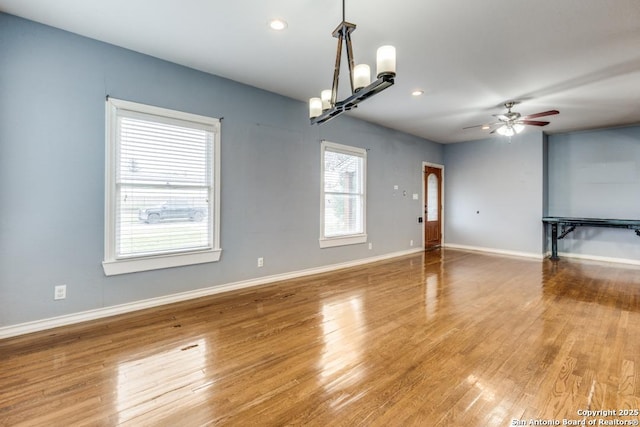 spare room featuring ceiling fan with notable chandelier and hardwood / wood-style floors