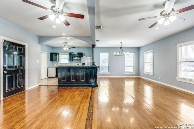 kitchen with dishwashing machine, ventilation hood, light hardwood / wood-style floors, an island with sink, and decorative light fixtures