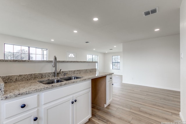 kitchen with light stone counters, sink, white cabinetry, and light wood-type flooring