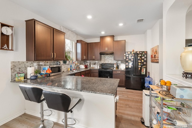 kitchen with kitchen peninsula, decorative backsplash, light hardwood / wood-style floors, and black appliances