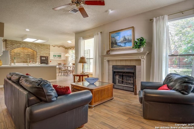 8907 Lost Bnd, San Antonio, TX 78240 - living room with ceiling fan, a fireplace, a textured ceiling, and light wood-type flooring