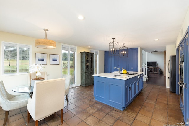 kitchen with pendant lighting, stainless steel fridge, blue cabinetry, and a center island with sink