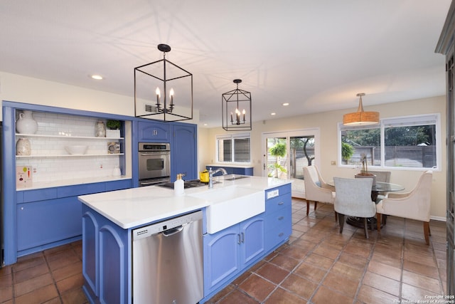 kitchen featuring appliances with stainless steel finishes, decorative light fixtures, blue cabinets, sink, and a center island with sink