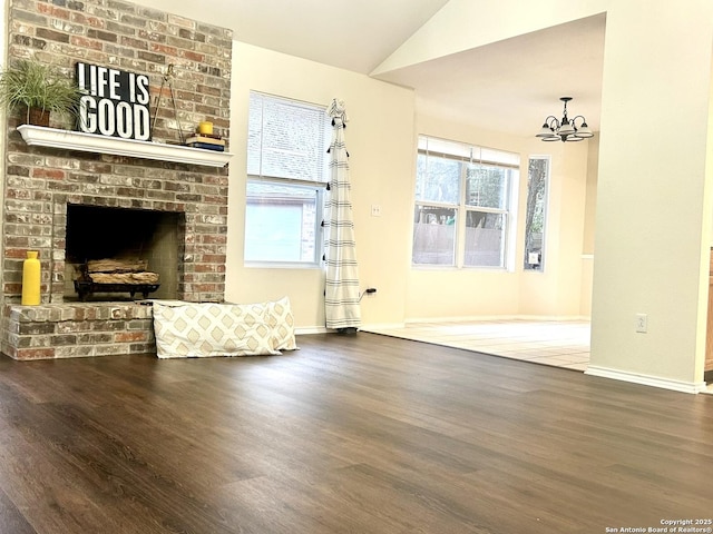 unfurnished living room with vaulted ceiling, a brick fireplace, hardwood / wood-style floors, and a chandelier