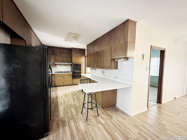 kitchen featuring a kitchen breakfast bar, kitchen peninsula, light hardwood / wood-style floors, and black appliances