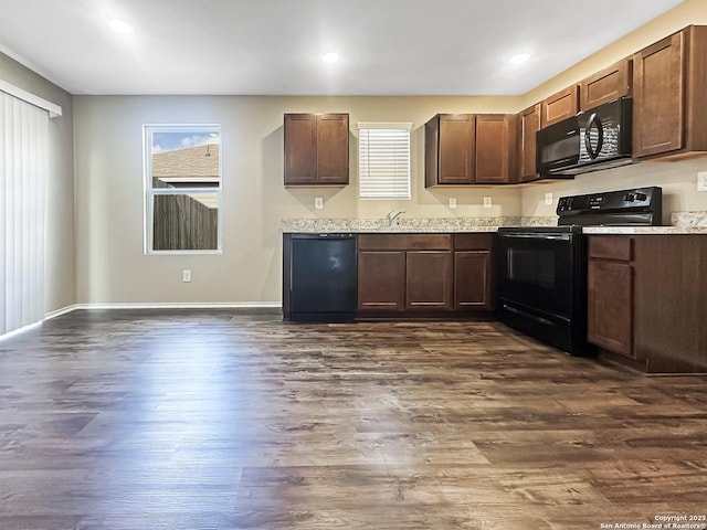 kitchen with sink, light stone counters, dark brown cabinetry, black appliances, and dark hardwood / wood-style flooring