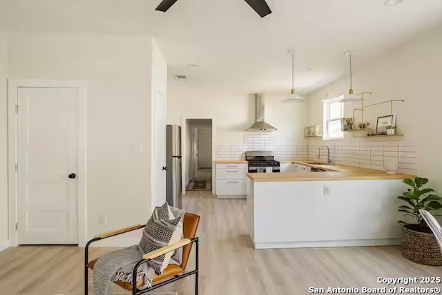 kitchen featuring white cabinetry, wall chimney exhaust hood, kitchen peninsula, hanging light fixtures, and stainless steel range oven