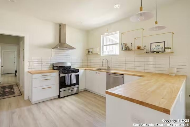 kitchen featuring stainless steel appliances, white cabinets, wall chimney range hood, sink, and kitchen peninsula