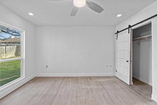 unfurnished bedroom with light hardwood / wood-style flooring, ceiling fan, a textured ceiling, a barn door, and a closet