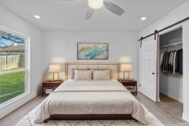 bedroom featuring ceiling fan, a barn door, light wood-type flooring, and a closet