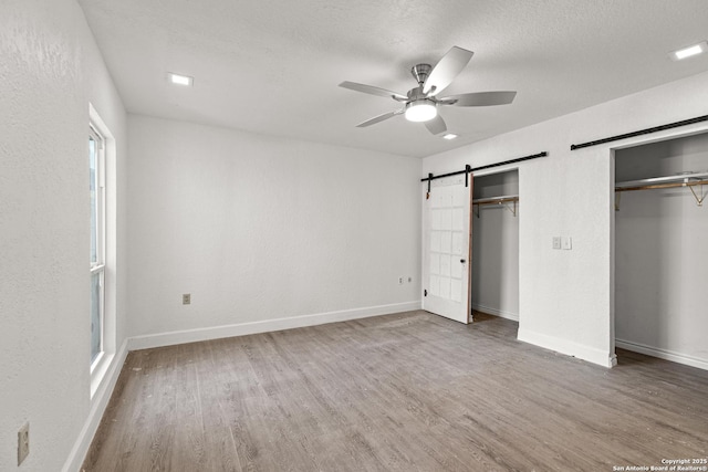 unfurnished bedroom with hardwood / wood-style flooring, ceiling fan, a textured ceiling, a barn door, and multiple closets