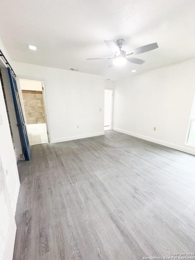 empty room with a barn door, hardwood / wood-style floors, and ceiling fan