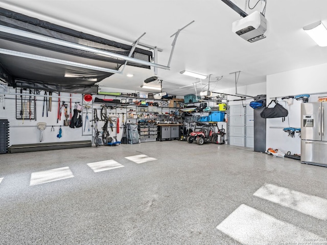 garage with a garage door opener, stainless steel fridge, and a workshop area