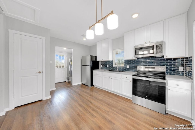 kitchen featuring sink, appliances with stainless steel finishes, white cabinets, pendant lighting, and backsplash