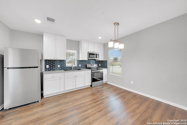 kitchen featuring sink, stainless steel appliances, hanging light fixtures, and white cabinets