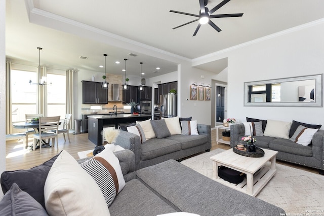 living room with ornamental molding, sink, ceiling fan with notable chandelier, and light hardwood / wood-style floors