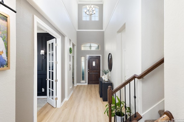 entryway featuring an inviting chandelier, a towering ceiling, and light hardwood / wood-style flooring