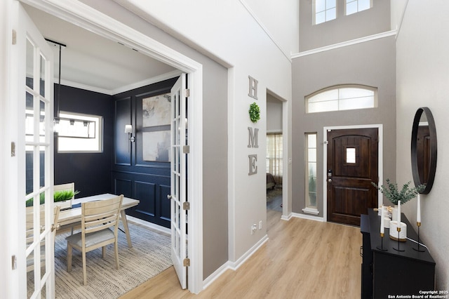 entryway featuring crown molding, a towering ceiling, and light hardwood / wood-style flooring