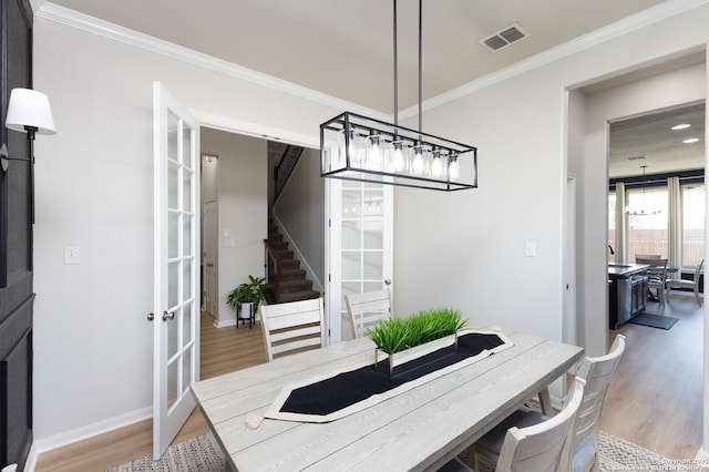 dining space featuring ornamental molding, light hardwood / wood-style flooring, and french doors