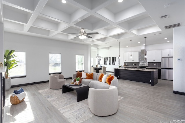 living room featuring coffered ceiling, sink, ceiling fan with notable chandelier, and light wood-type flooring