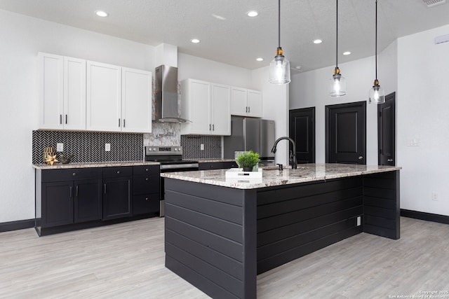 kitchen featuring wall chimney exhaust hood, white cabinetry, appliances with stainless steel finishes, pendant lighting, and light stone countertops