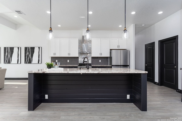 kitchen with white cabinets, light stone countertops, stainless steel refrigerator, and a large island with sink