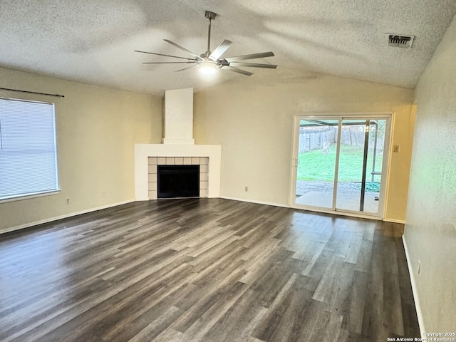 unfurnished living room with vaulted ceiling, dark hardwood / wood-style floors, a tiled fireplace, ceiling fan, and a textured ceiling