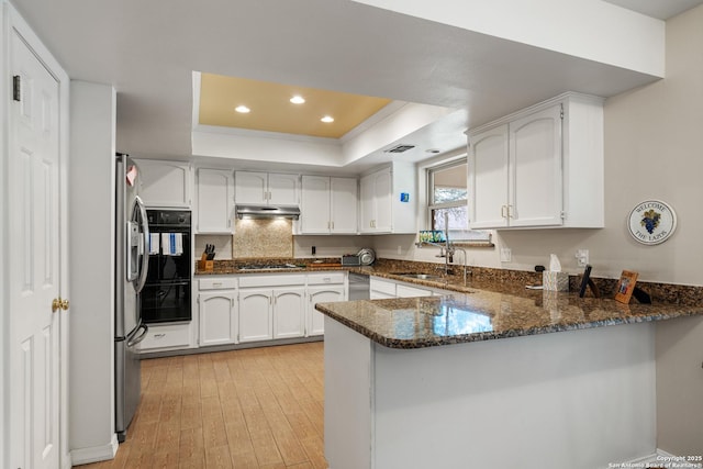 kitchen featuring white cabinetry, kitchen peninsula, black appliances, a tray ceiling, and dark stone countertops