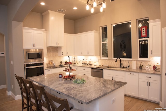 kitchen with a breakfast bar, sink, light stone counters, a center island, and appliances with stainless steel finishes