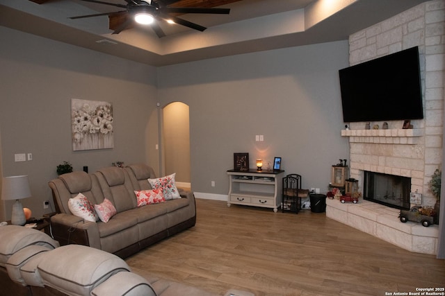 living room with hardwood / wood-style flooring, ceiling fan, a fireplace, and a tray ceiling