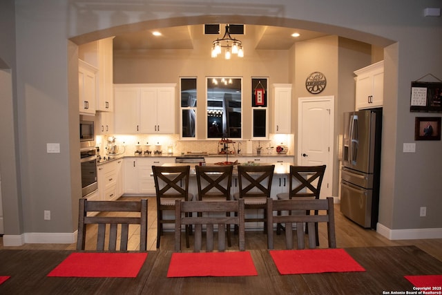 kitchen with tasteful backsplash, hanging light fixtures, white cabinets, and appliances with stainless steel finishes