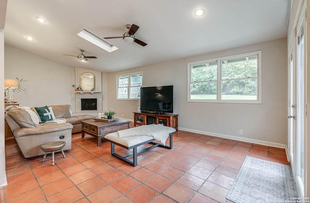 living room featuring ceiling fan, tile patterned floors, a fireplace, and vaulted ceiling with skylight